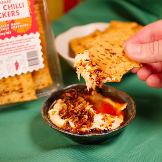Person dipping a cracker into a bowl of dip with a box of crackers in the background.