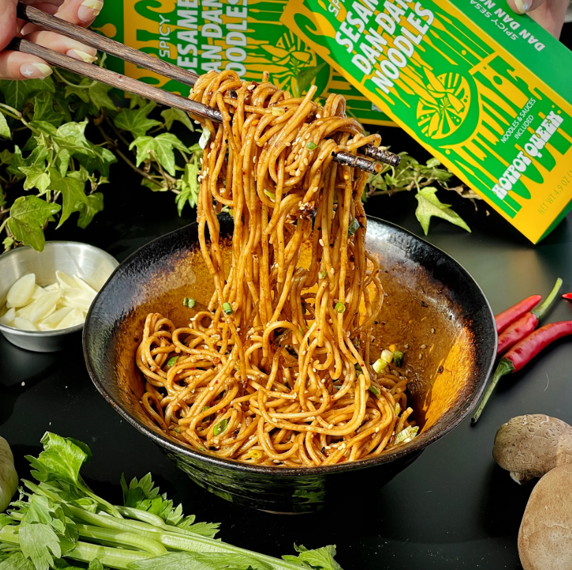 Noodles being lifted with chopsticks from a bowl with a noodles box in the background