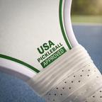 Close-up of a pickleball paddle with 'USA Pickleball Approved' text on a blurred background