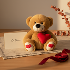 Brown teddy bear with a red heart, sitting on a wooden surface with a card and ribbon.