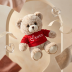 Teddy bear wearing a red shirt with 'XOXO' on it, surrounded by heart-shaped decorations.