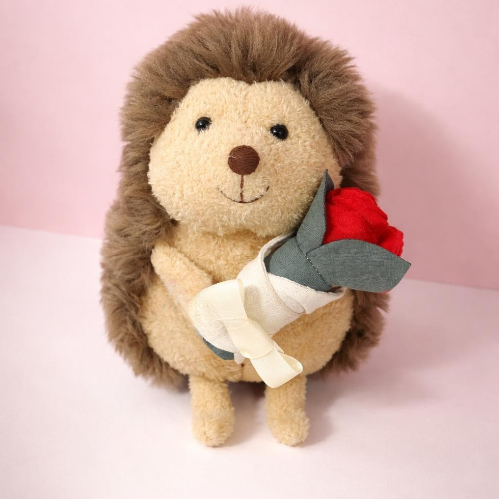 Stuffed hedgehog toy holding a red rose on a pink background